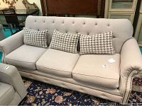 Front view of the light gray upholstered couch showing the seat cushions and three houndstooth pillows.
