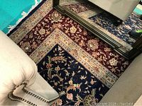 Photo showing corner and border detail of the rug with floral pattern and furniture edges.