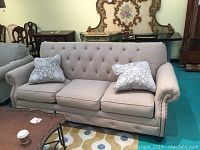 Front view of beige upholstered couch with two patterned pillows in a room with other furniture