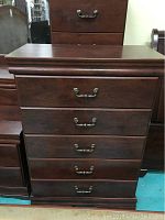 Front view of the dark wood chest of drawers showing five drawers with metal handles.