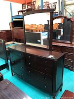 Full front view of dark wood dresser with mirror in a warehouse setting showing all drawers and mirror attached.