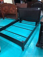 Photo showing side angle of black metal queen bed frame with upholstered headboard and footboard
