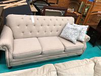 Front view of beige upholstered sofa showing tufted back, rolled arms, seat cushions and bun feet