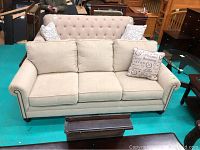 Front view of beige three-seat sofa with three seat cushions, rolled arms with nailhead trim, and two decorative pillows.
