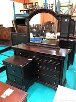 Wooden dresser with six drawers and large attached arched mirror, showing dark finish.