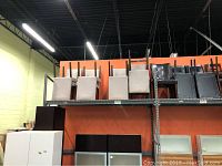 Eight beige upholstered chairs stacked on top shelf in warehouse.