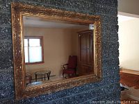 Front view of gold painted mirror showing ornate floral frame detail and reflection of room interior.