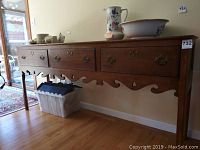 Front view of the wood sideboard showing three drawers with brass handles and carved trim at the bottom edge, with some ceramic items on top (not included).