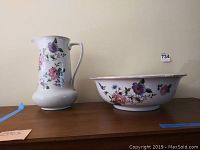 Pitcher and bowl set side by side on wooden surface against plain wall, showing floral pattern and size