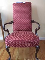 Front view of a tall back chair upholstered in red diamond lattice fabric with curved wooden arms and cabriole legs.