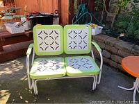 Front view of two-seat bench glider with green frame and white decorative panels in outdoor setting