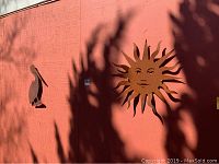 Two rusted metal wall art pieces mounted on a wall: a pelican and a sun with face and rays.