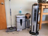 Photo of Shark floor sweeper, micro cut shredder with shredder lubricant, vertical tower fan or humidifier, globe and small trash can arranged against a wall.