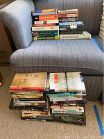 Books stacked on a grey upholstered chair, showing the variety of titles and genres included in the lot.
