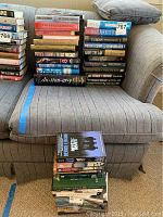 Full view of a large stack of books on a striped armchair with a cushion showing a variety of titles and authors