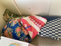 Shows two comforters stacked together, one featuring large orange and pink floral design on blue, and the other a green floral comforter partially visible.