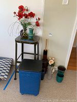Photo showing blue woven vintage hamper, tall metal stool, and surrounding decor including vases and artificial flowers