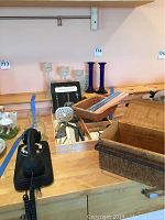 Photo displaying the vintage black rotary phone, a large wooden rectangular box, wicker basket with rolled fabric, bar tool set including a strainer and spoon, and two pairs of candlesticks.