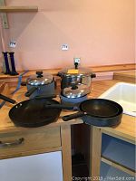 Full shot of Circulon pots and pans including two pots with lids, one large pot with lid, and two frying pans with black non-stick interiors.