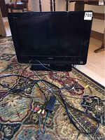 Front view of Sony Bravia television on carpet with cables attached, showing screen and bezel in good condition.