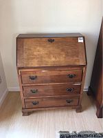 Front view of vintage wooden secretary desk with closed drop-front and three drawers.