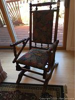 Front view showing the rocking chair with floral upholstered seat and back with turned wooden arms and spindles.