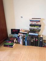 Photo showing a large collection of hardcover books stacked in two piles on the floor against a white wall, including travel and adventure-themed titles.