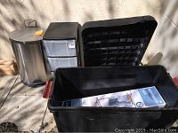 Photo of two large black storage containers, stainless steel trash can, and plastic drawer unit.