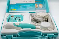 Turquoise and white handheld laser device and control unit with coiled power cord inside carrying case.