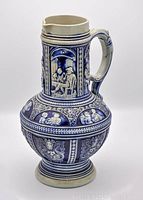 Full view of blue ceramic jug with relief molded decorations and handle.