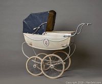 Side view of vintage Silver Cross baby carriage showing cream body, navy hood, rose enamel medallion, large spoked wheels, and metal frame.
