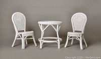 Photo showing white wicker child's table and two matching wicker chairs against a plain backdrop
