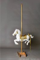 Full profile view of the white and gold carousel horse on pole with wooden base