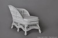 Side and front angled view of child's white wicker fainting couch showing curved back, woven detailing, and lower wicker skirt with legs on casters.