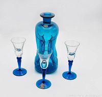 Full view of the blue glass decanter with three matching stemware cordial glasses showing overall design and color.