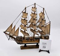 Front and side view of the wooden sailing ship model with multiple cream-colored sails and detailed rigging mounted on a rectangular wooden stand with label.