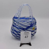 Front angled view of the Rossi art glass basket showing the blue, white, and lime green criss-cross pattern, clear handle, and original Rossi sticker on the side.