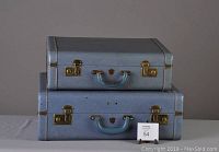 Front view of stacked matching blue vintage suitcases with blue handles and gold hardware on table against plain background.
