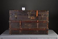 Front view of vintage steamer trunk showing original hardware, leather straps (one broken), and metal corner protectors.