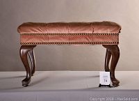 Front view of the vintage footstool showing padded leather seat and nailhead trim with cabriole wooden legs.