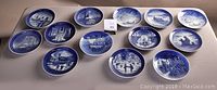 Overview of all 13 Royal Copenhagen blue and white collector plates arranged on a table showcasing different maritime and winter scenes.