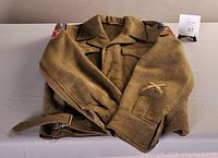 Folded view of the green wool military jacket showing sleeves, belt, and shoulder patches.