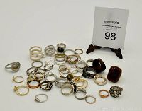 Photo showing about 30 assorted costume jewellery rings in various metal and color finishes, including gold-tone, silver-tone, and copper-tone with some rings set with faux stones or decorative details.