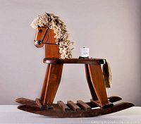 Side view of the whole vintage wooden rocking horse showing the body, base, and yarn mane and tail