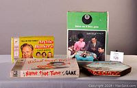 Four vintage board games displayed including All in the Family Archie Bunker card game, Name That Tune, Marble Checkers, and Behind the 8 Ball game.