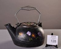 Side angle view of vintage cast iron kettle showing floral hand-painted decoration and metal coil handle replacement.