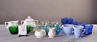 Photo shows multiple cream and sugar sets displayed together including green, blue, white porcelain, and glass sets arranged on a neutral surface.