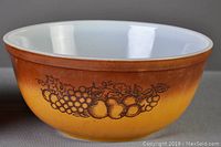 Yellow to brown two-tone Pyrex mixing bowl with Old Orchard fruit pattern on the exterior side, white interior, showing wear and patina consistent with vintage use.