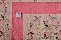 Close-up of quilt border showing pink fabric with hand stitching and appliqued leaves and flowers on a cream background.