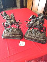 Pair of metal rider sculptures on wooden bases viewed frontally on red cloth